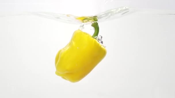 Желтая паприка брызгает в воду в медленном темпе — стоковое видео