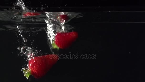 Tři strawberryes šťávy do vody v slowmotion — Stock video