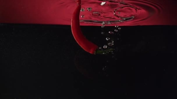 Перець чилі розбризкується у воді в сповільненні — стокове відео