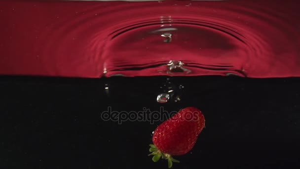 Daling van de aardbei in water in slowmotion — Stockvideo