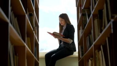 kız öğrenci bir pencere pervazına kütüphanede üzerine bir kitap okuma. Yakın çekim