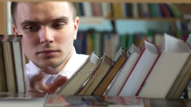 O rapaz escolhe um livro na biblioteca. fechar, seleciona o desejado — Vídeo de Stock