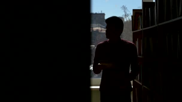 Silhouette kille lägger boken på sin plats i biblioteket. det flyttar kameran — Stockvideo
