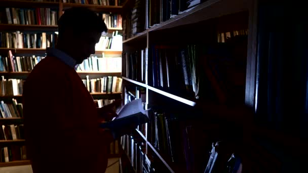 De man zet het boek in zijn plaats in de bibliotheek. Bladeren door het boek — Stockvideo