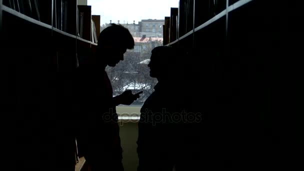 Silhouette studente universitario parlare tra le librerie in una biblioteca, compagno sorridente . — Video Stock