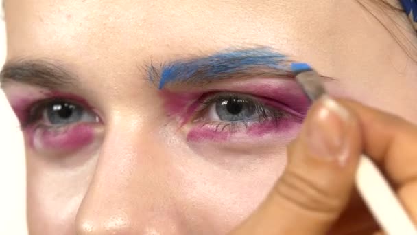 Maquillaje de ojos mujer aplicando sombra de ojos, haciendo exótico, dos ojos, ceja azul, de cerca, en blanco — Vídeo de stock