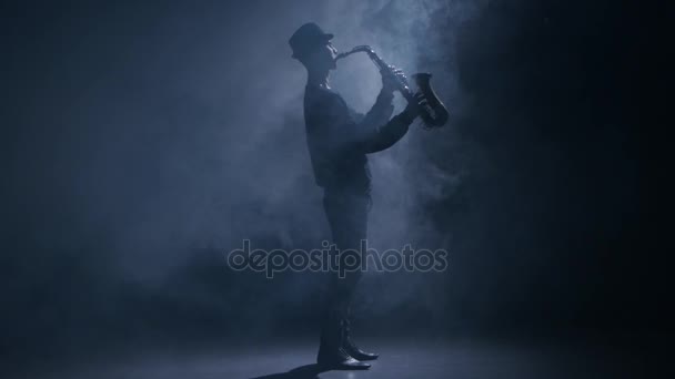 Σαξοφωνίστας παίζει ένα μουσικό όργανο σε ένα σκοτεινό στούντιο καπνιστή — Αρχείο Βίντεο