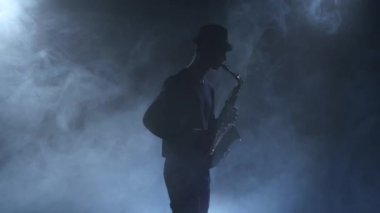 Genç jazzman saksofon çalıyor. Işık ile karanlık dumanlı studio