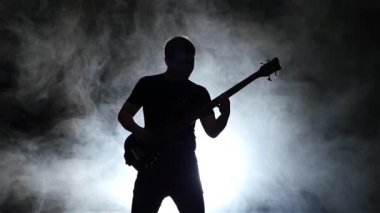 Ağır çekim. Siluet bas gitarist adam duman. Siyah arka plan