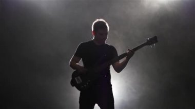 Duman ile koyu arka plan. Adam siyah bas gitar çalmaya