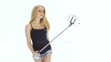 Beyaz arka plan. Sarışın cep telefonunuzda fotoğraf yapar selfie stick kullanarak