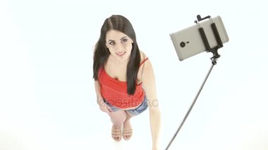 Esmer kız selfie fotoğrafları bir monopod kullanarak yapıyor. Beyaz arka plan