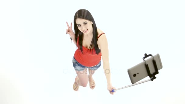 Meisje doet selfie foto's met behulp van een monopod. Witte achtergrond — Stockvideo