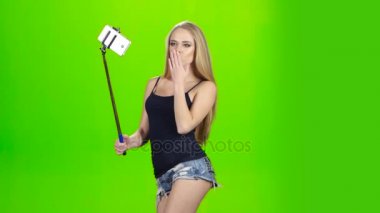 Sarışın kız çeşitli fotoğraflar selfie stick kullanarak yapar. Yeşil ekran