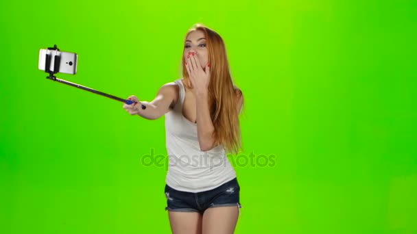 Redheaded girl makes various photos using selfie stick. Green screen — Stock Video