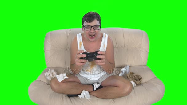 Игрок играет в видеоигры с геймпадом, сидящим на грязном диване — стоковое видео
