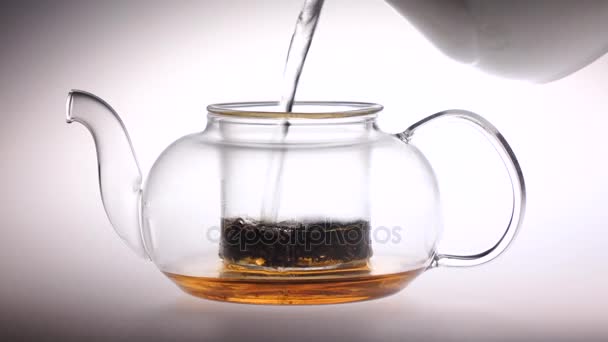 El agua hirviendo se vierte en una tetera de vidrio con hojas de té — Vídeo de stock