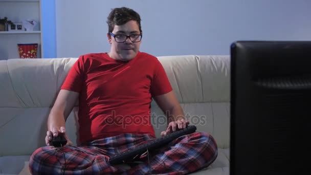 Забавный человек, играющий в компьютерную игру, сидя на большом диване — стоковое видео