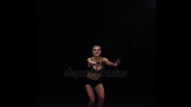 Acrobat girl jumps bending the knees. Slow motion. Black background — Stock Video