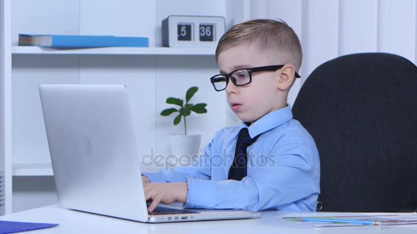 Heldere jongen typt op een laptop en het schrijft zelf naar het blad — Stockvideo