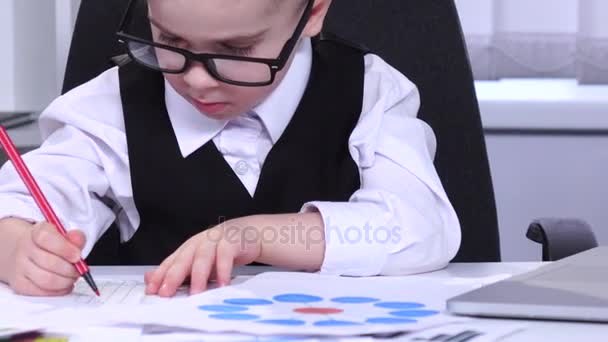 Little boy businessman looking at charts and data are entered into a laptop — Stock Video