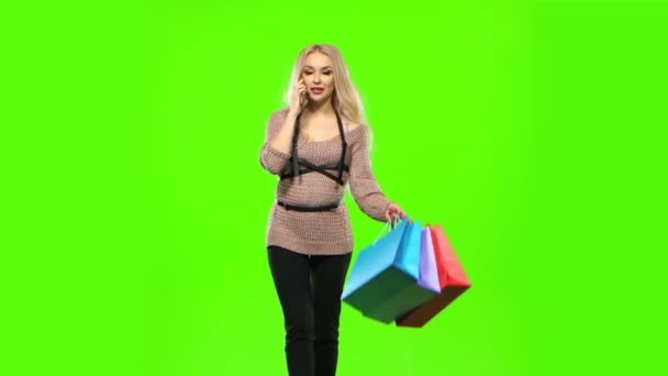 Blond flicka bär ett flerfärgat paket, talar i telefon och ler sött. Grön skärm — Stockvideo