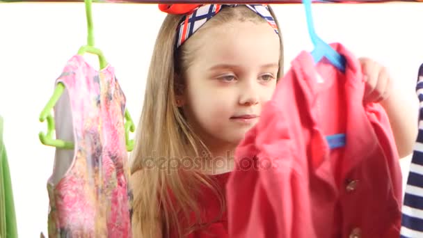 Μικρό κορίτσι στο κατάστημα επιλέγει ρούχα και βρίσκει κατάλληλο. Λευκό φόντο — Αρχείο Βίντεο
