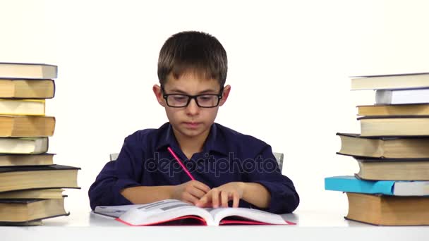 El chico se sienta a la mesa hojeando el libro. Fondo blanco — Vídeos de Stock