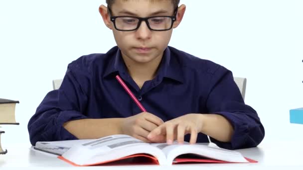 Pojke sitter vid ett bord spela in något i hennes anteckningsbok och flips genom boken. Vit bakgrund — Stockvideo