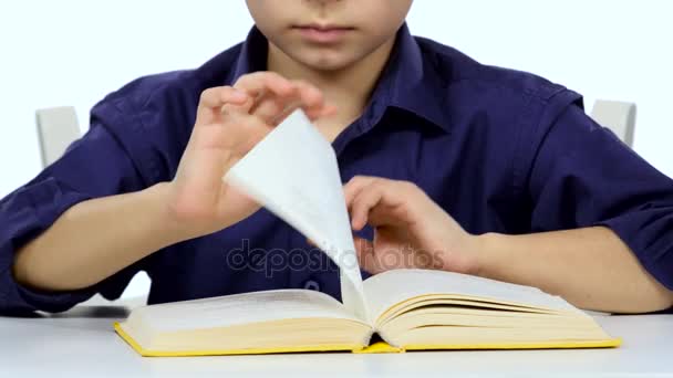 Liten pojke sitter vid ett bord och läser intressanta bok långsamt. Vit bakgrund. Närbild — Stockvideo