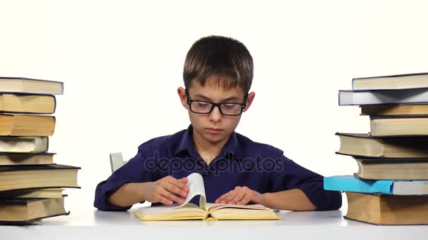 El chico se sienta a la mesa hojeando las páginas de un libro. Fondo blanco . — Vídeos de Stock