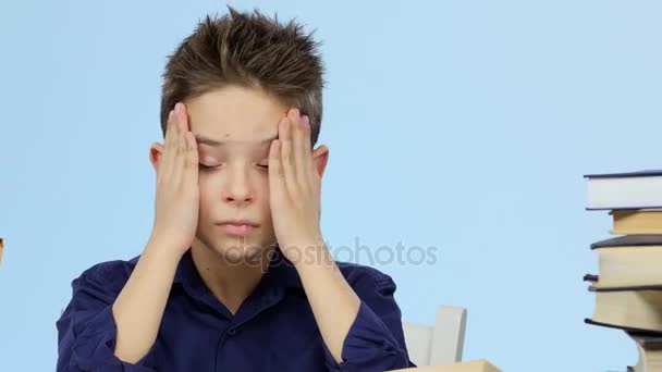 Trött pojke sitter vid ett bord för en bok somnar och vaknar upp. Blå bakgrund. Närbild — Stockvideo