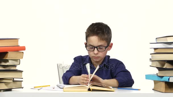 Le petit garçon s'assoit à une table et lit le livre lentement. Fond blanc — Video