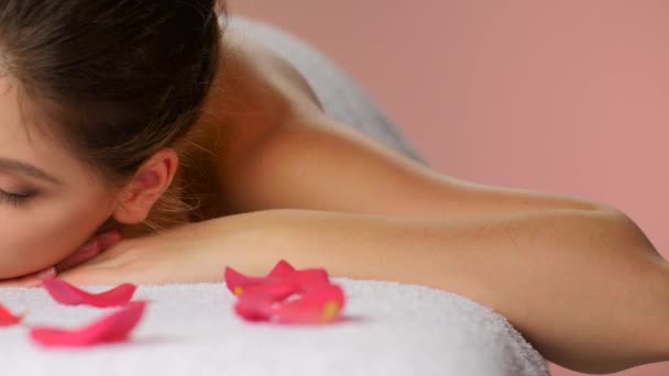 Chica relajante después de masaje acostado en toallas con pétalos de rosa — Vídeos de Stock