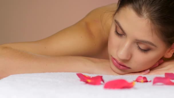 Vrouw ontspannen na massage liggend op handdoeken met rozenblaadjes — Stockvideo