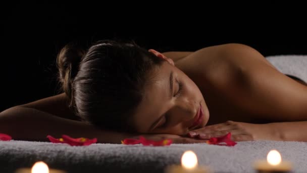 Chica duerme después de tratamientos de spa en pétalos de rosa, velas encendidas — Vídeos de Stock