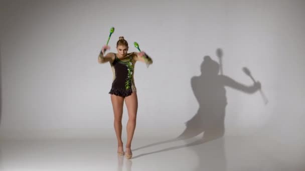 Ритмичная гимнастка, стоящая на коленях и держа булаву, делает акробатические движения. Белый фон — стоковое видео