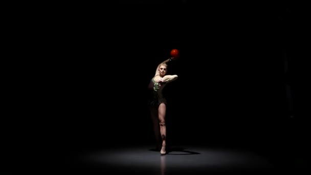 Гимнаст с мячом в руках делает акробатические движения. Чёрный фон — стоковое видео