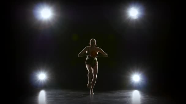 Gimnasta flexible lidera la pelota en su cuerpo. Fondo negro. Luz trasera — Vídeos de Stock