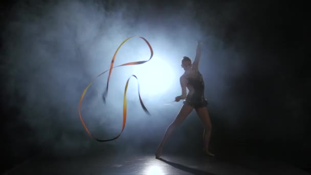 Gymnast with a ribbon in the hands circling in the smoke. Black background. Light rear. Silhouette — Stock Video