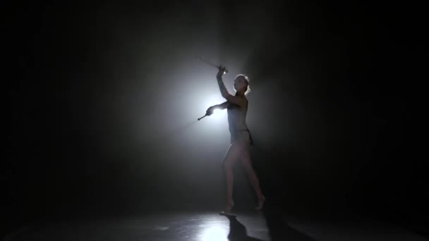 Chica gimnasta con maza en la mano giran en torno a él. Fondo negro. Luz trasera. Silueta — Vídeo de stock