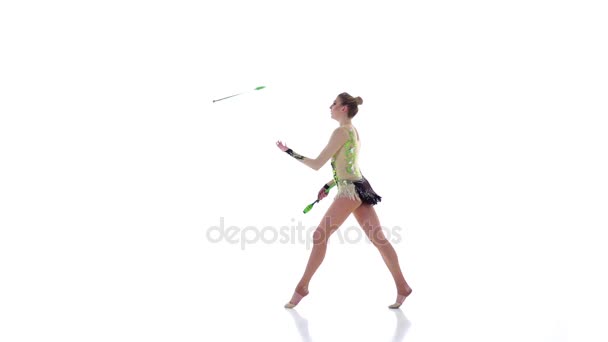 Κορίτσι γυμναστής με ρόπαλο στο χέρι περιστρέφονται γύρω από αυτόν. Λευκό φόντο. Αργή κίνηση — Αρχείο Βίντεο
