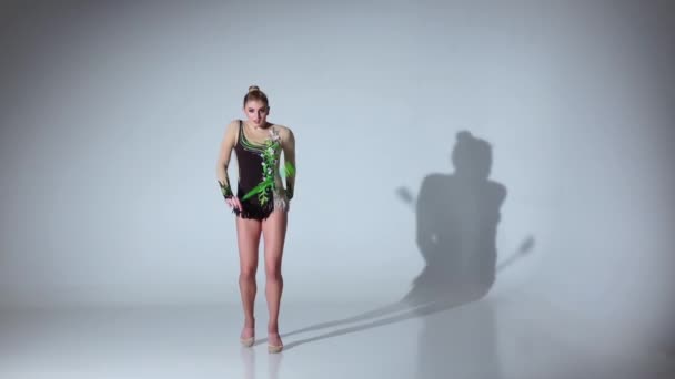 Rhythmische Turnerin kniet und hält ihre Keule und macht akrobatische Bewegungen. weißer Hintergrund. Zeitlupe — Stockvideo
