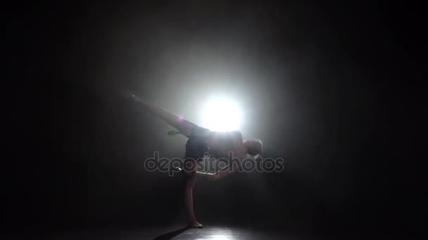 Дівчина-гімнастка з мрією в руці обертається навколо нього. Чорний фон. Світло позаду. Силует. Повільний рух — стокове відео