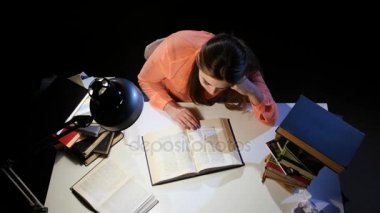 Kız bir kitap aracılığıyla leafing ve masada uykuya dalmak. Siyah arka plan. Yukarıdan görüntülemek