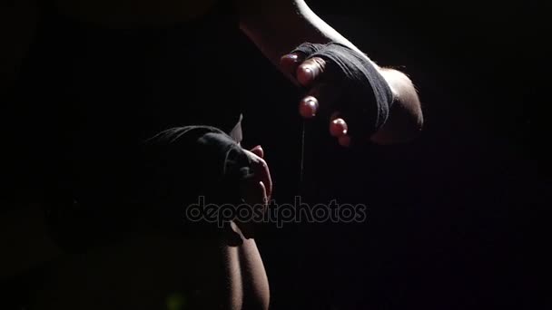 ボクサーは彼の手の特別な包帯を交わしています。シルエット。黒の背景。側面図です。クローズ アップ。スローモーション — ストック動画