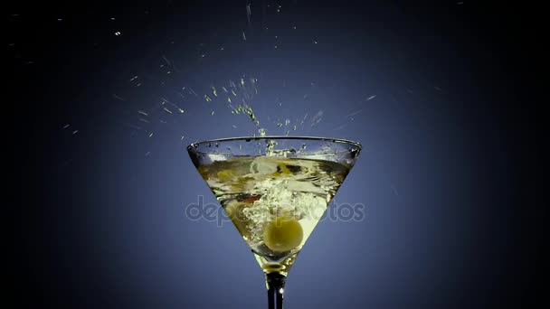 Two olives fall into tall martini glass. Black background — Stock Video