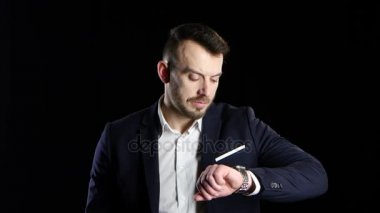 İşadamı endişeyle bekliyor ve saatine görünüyor. Siyah arka plan