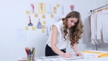 Moda Tasarımcısı skeçler gülümser ve yeni bir koleksiyon için tatlı tatlı çizer