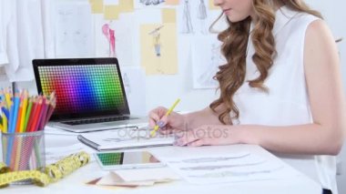 Moda Tasarımcısı yeni bir koleksiyon için skeçler çizer ve bilgisayar bakar